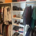 Walk-in closet with handbags on shelves above hanging clothes