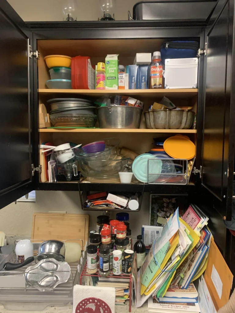 Kitchen cabinet before organizing, crowded with containers