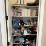 Narrow storage closet with paper goods and cleaning supplies on shelves