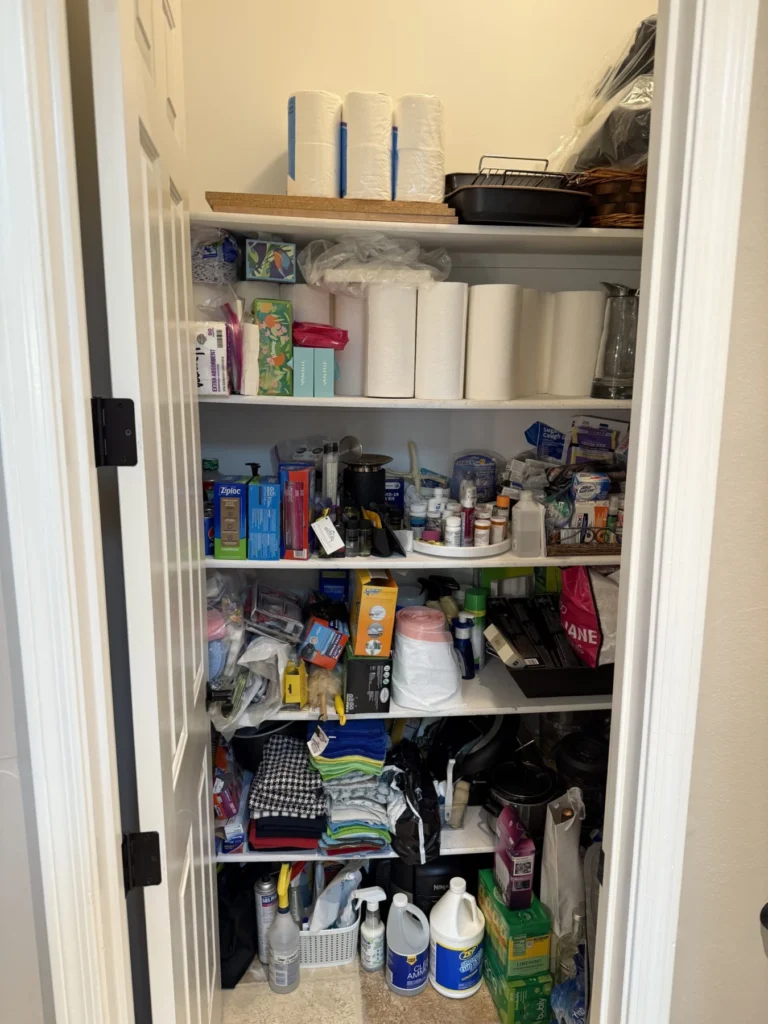 Narrow storage closet with paper goods and cleaning supplies on shelves