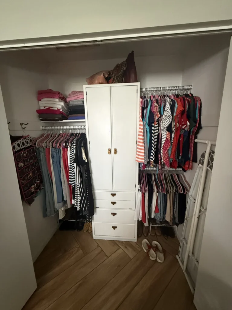 Reach-in closet with clothes hung around a white dresser