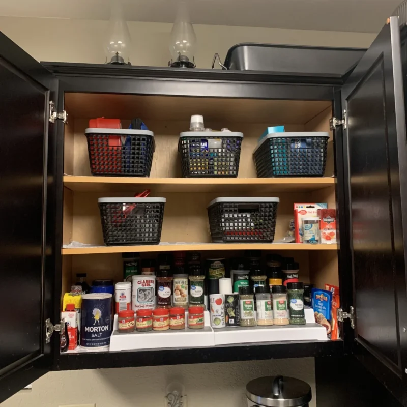 Kitchen cabinet after organizing, with spices and supplies in bins