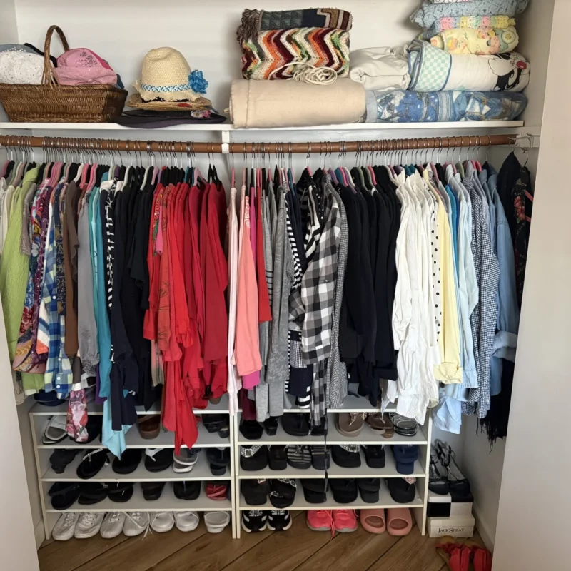 Unpacked closet with shoes on a rack below hanging clothes